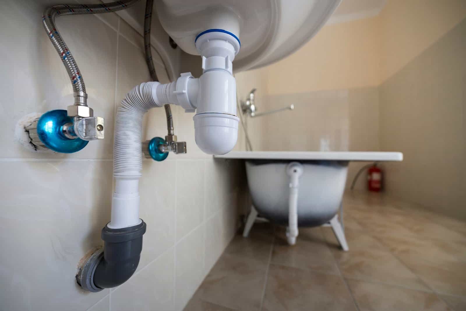 Plumbing pipes and drain under sink in bathroom for water damage restoration.