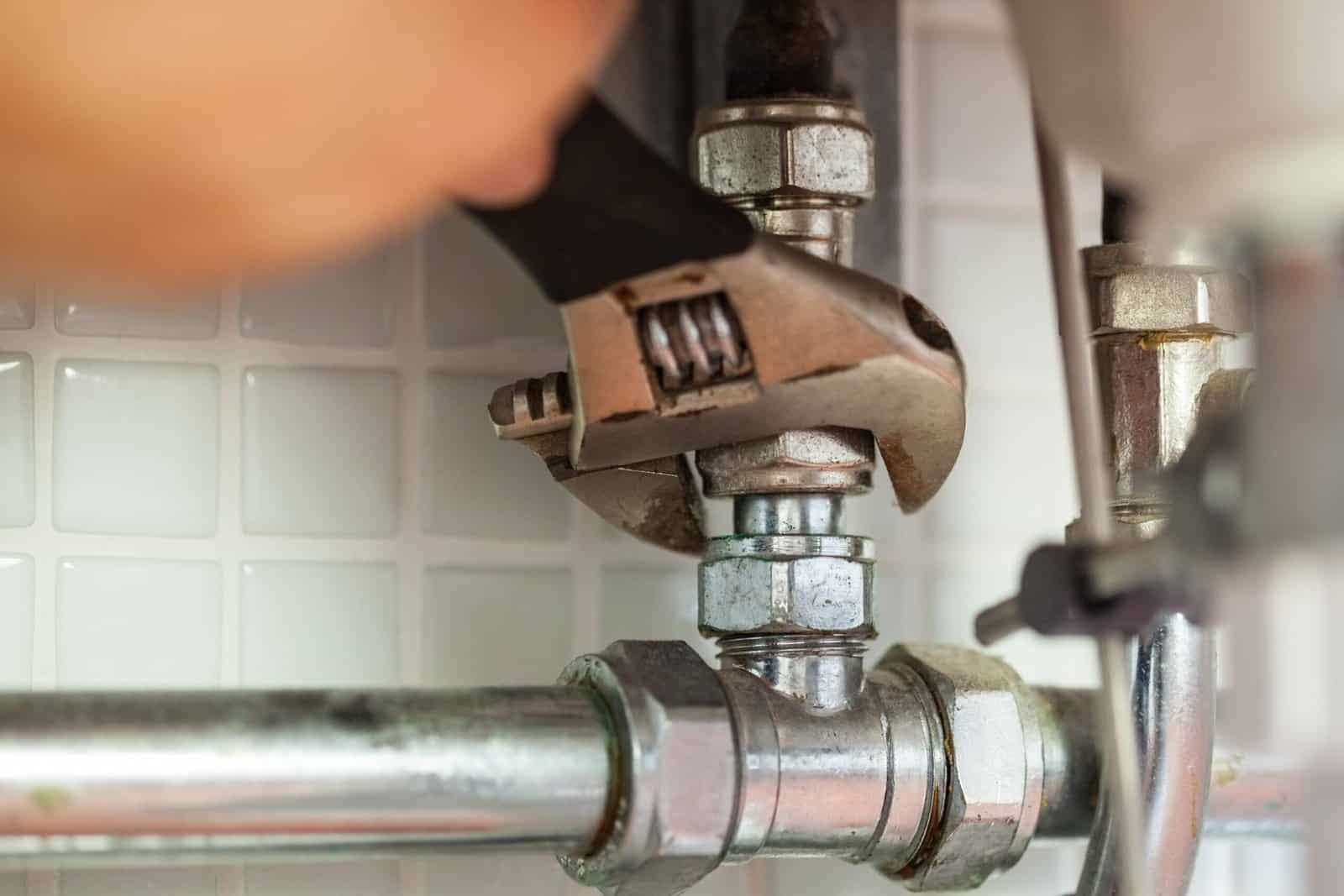 Technician repairing water pipe with adjustable wrench in plumbing system.