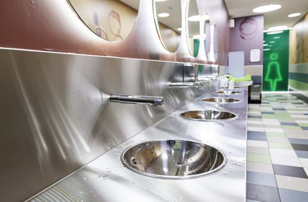 Public restroom with stainless steel sinks and colorful decor.